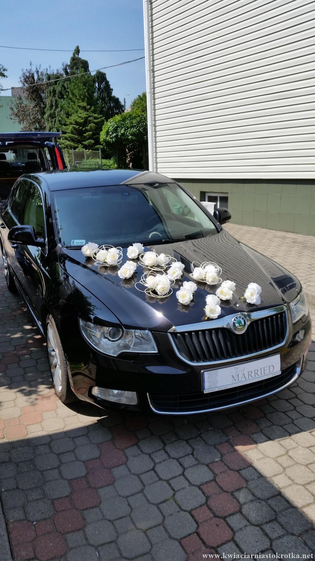 Białe auto udekorowane kwiatami i wstążkami na ślub