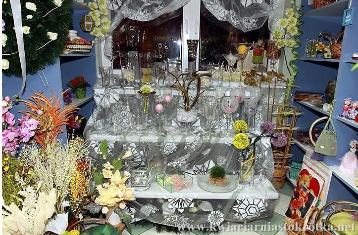 Kwiaty w donicach i koszach ustawione przy wejściu do kwiaciarni